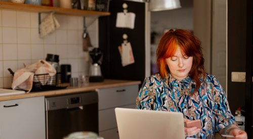 Dame som sitter ved kjøkkenbordet og betaler regninger, illustrasjonsfoto.