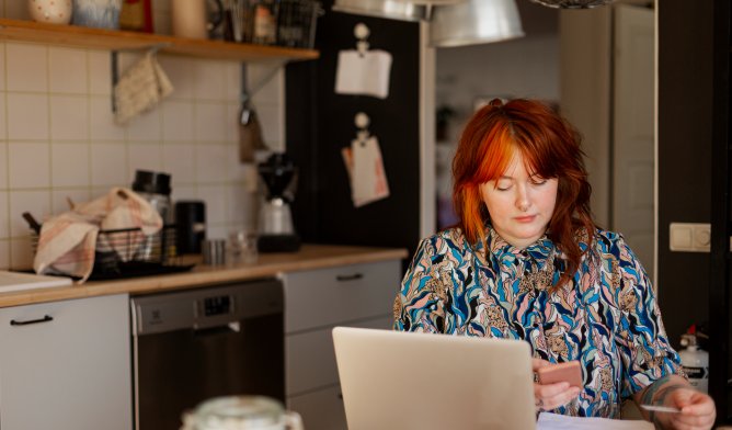 Dame som sitter ved kjøkkenbordet og betaler regninger, illustrasjonsfoto.